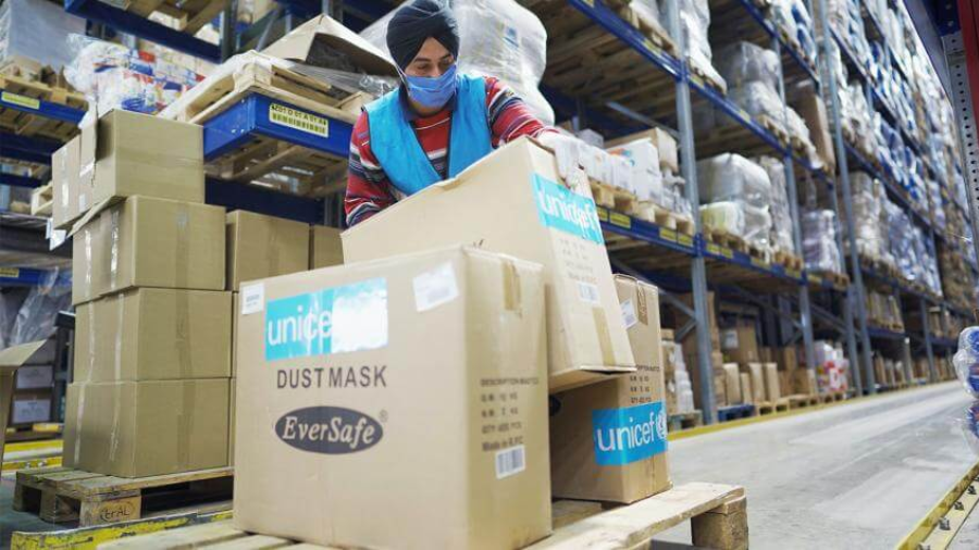 Man wearing mask, loading cartons onto a pallet inside a warehouse